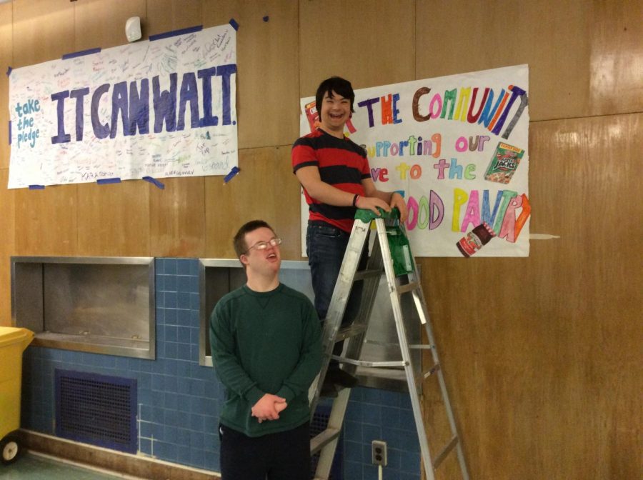 Timothy LaBudde (21) on left and Max Vanderwilden (21) on right hang up the poster announcing the food drive.