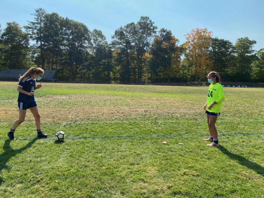 Two players from the Girls Soccer team playing pass, wearing masks and staying six feet apart